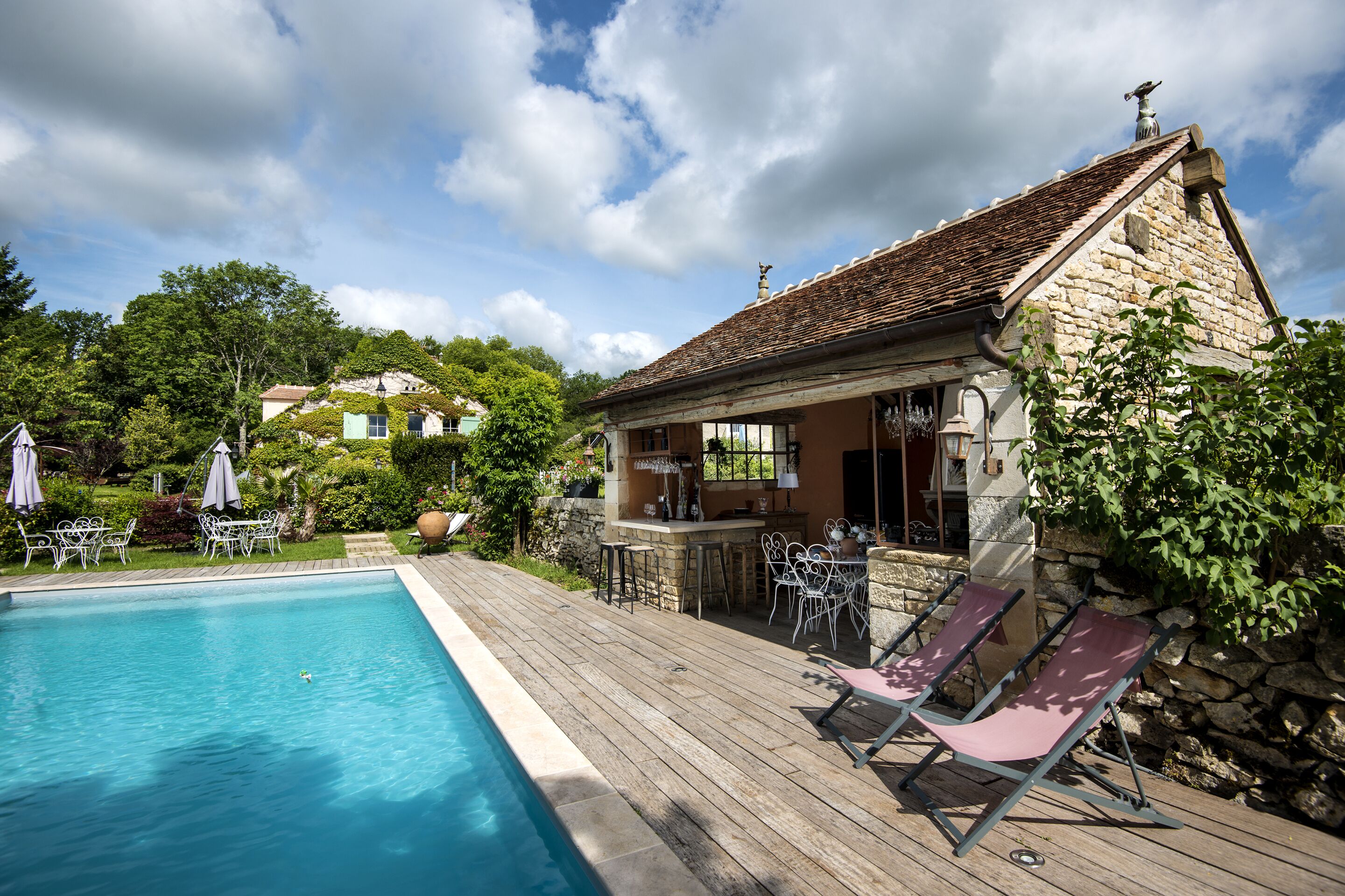 A poolside area with a stone building, outdoor seating, and a clear sky.