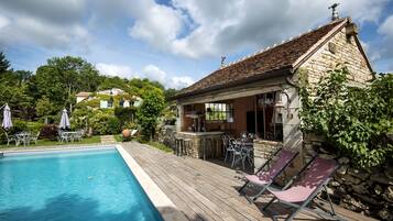 A poolside area with a stone building, outdoor seating, and a clear sky.
