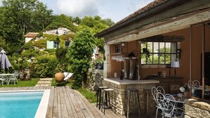 A poolside area with a bar, outdoor seating, and a view of a hillside. - Le Domaine des Carriers - Gîtes (Chevroches)