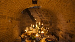 A dimly lit stone-walled room with a table set for dining, featuring candles, wine bottles, and a bowl of fruit. - Le Domaine des Carriers - Gîtes (Chevroches)