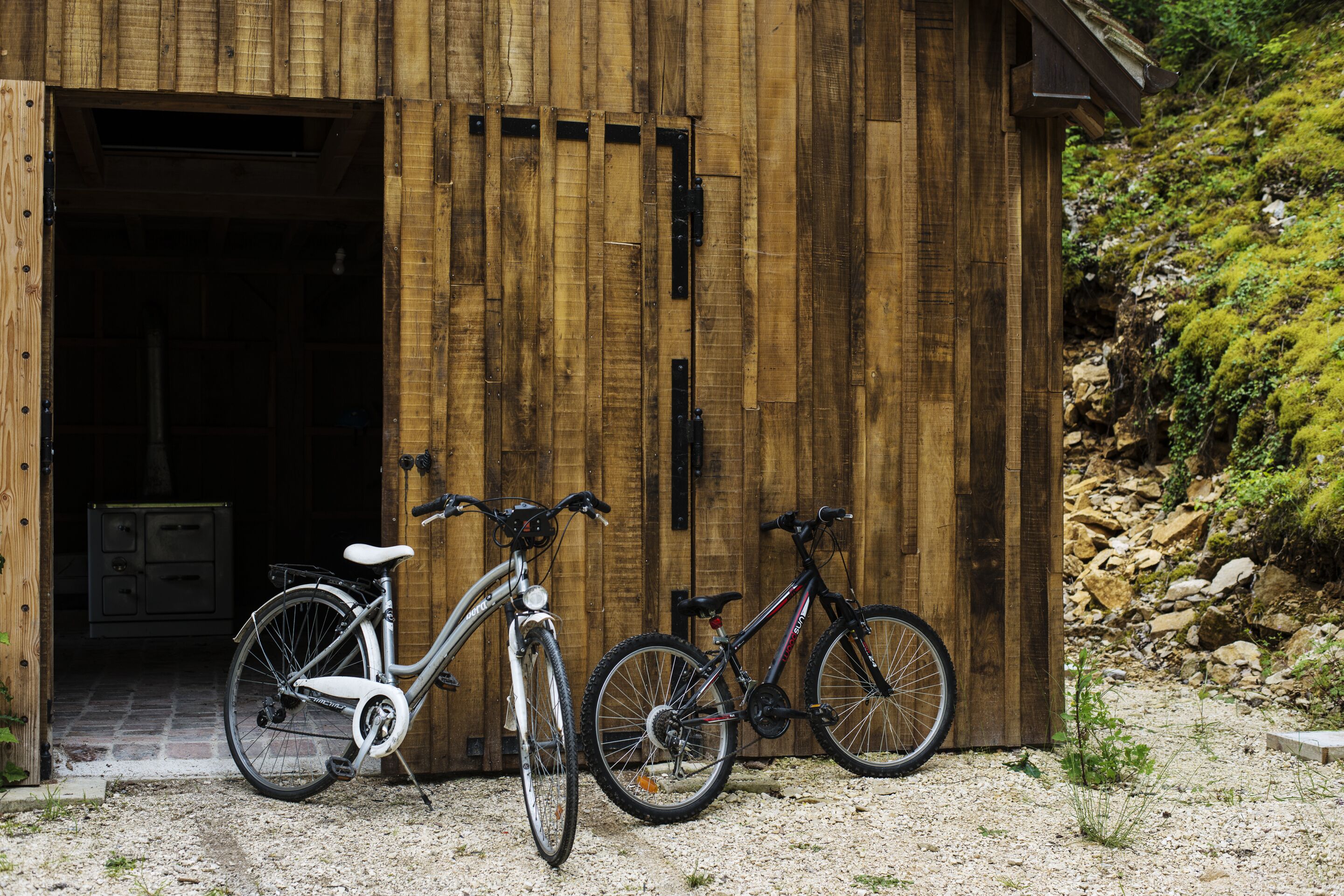 A wooden building with a door, two bicycles parked in front, and a gravel ground.