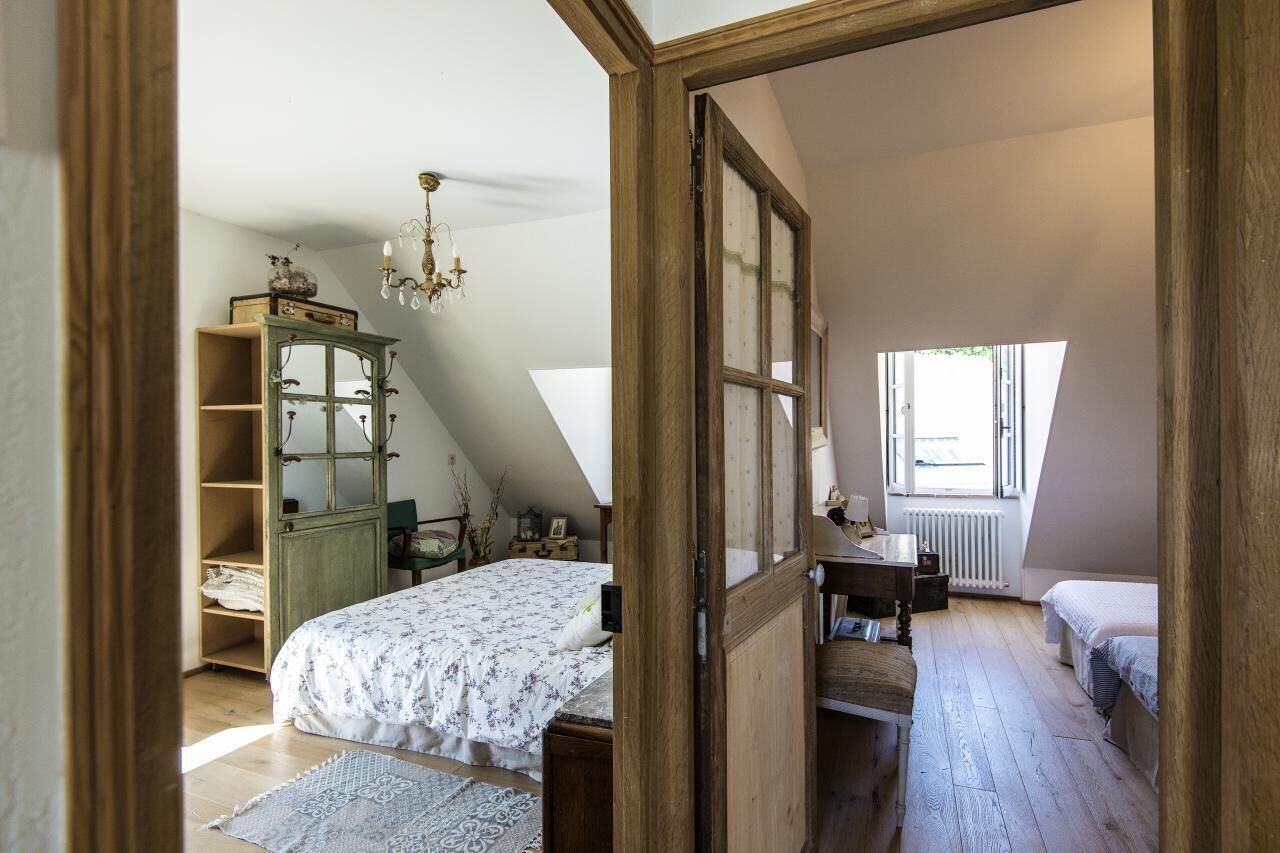 Een slaapkamer met een schuine kap, een houten garderobe, een bed met een bloemenlaken, een kleine tafel en een raam met uitzicht.