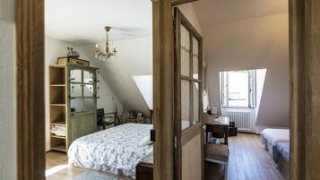 Een slaapkamer met een schuine kap, een houten garderobe, een bed met een bloemenlaken, een kleine tafel en een raam met uitzicht.