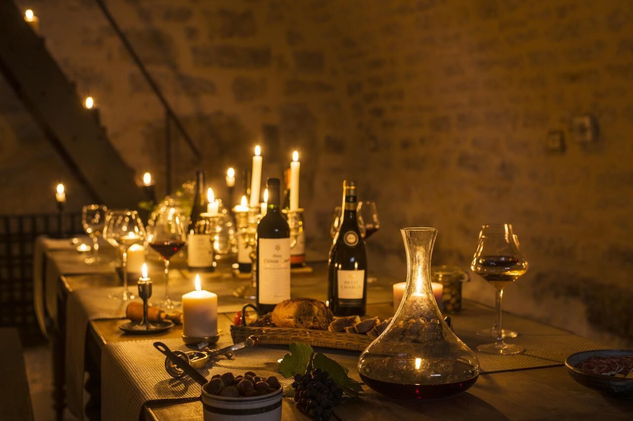 A long table set with wine bottles, glasses, candles, and food items, suggesting a dining or tasting event.