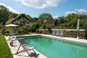 A swimming pool with lounge chairs, a patio area, and stone walls.