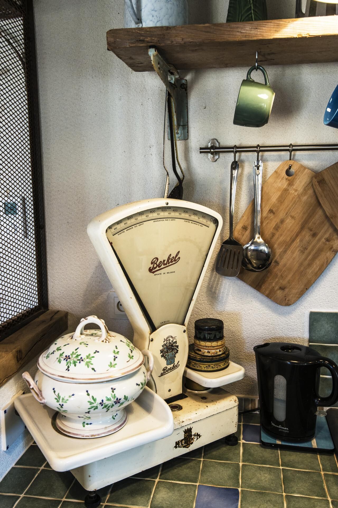 Eine Vintage-Küche mit einer weißen Waage, einem Holzschneidebrett, einer grünen Tasse und einer schwarzen Kaffeekanne.
