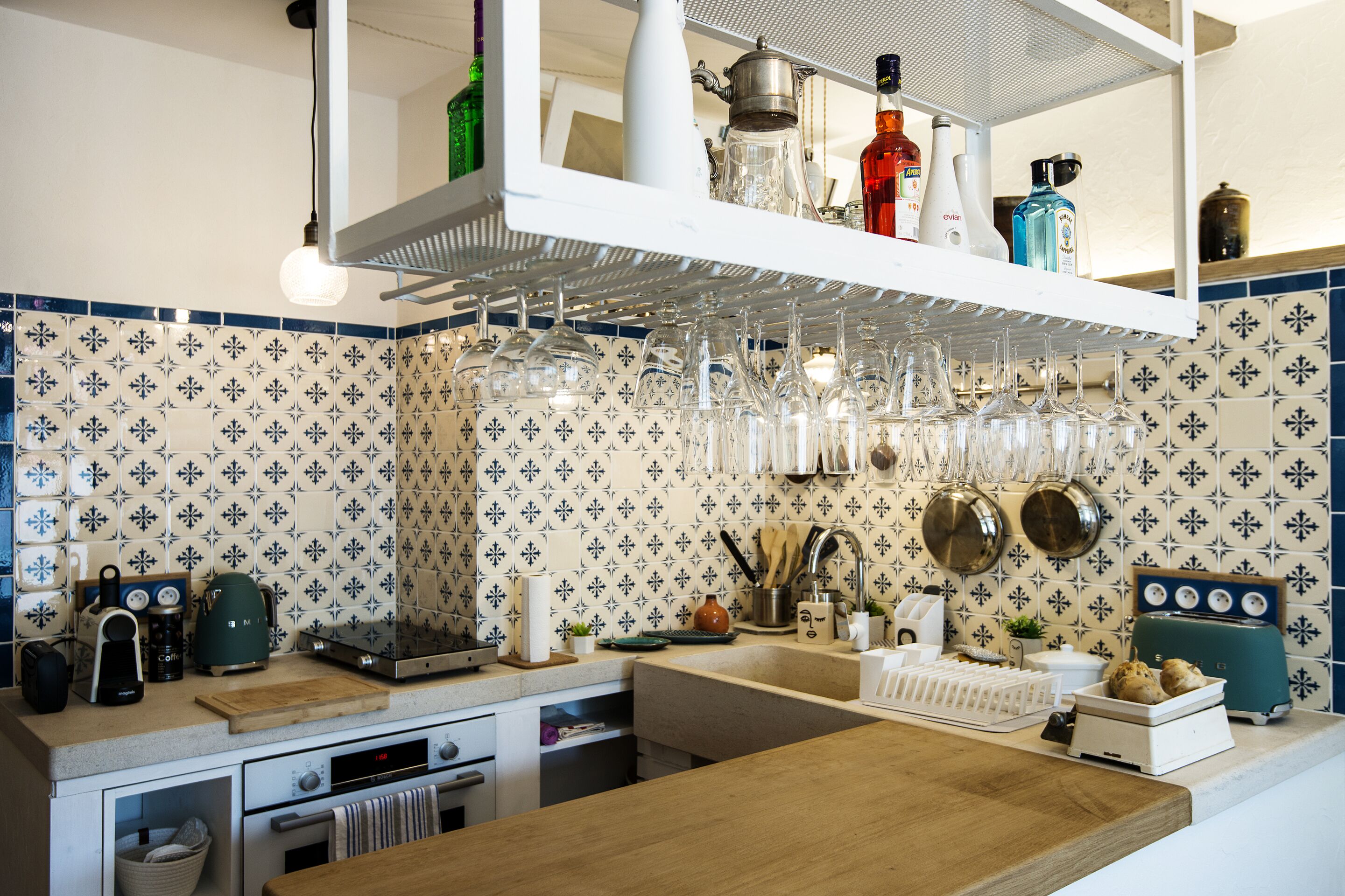 A kitchen with a tiled backsplash, a wooden countertop, a built-in oven, and a hanging rack with glassware.