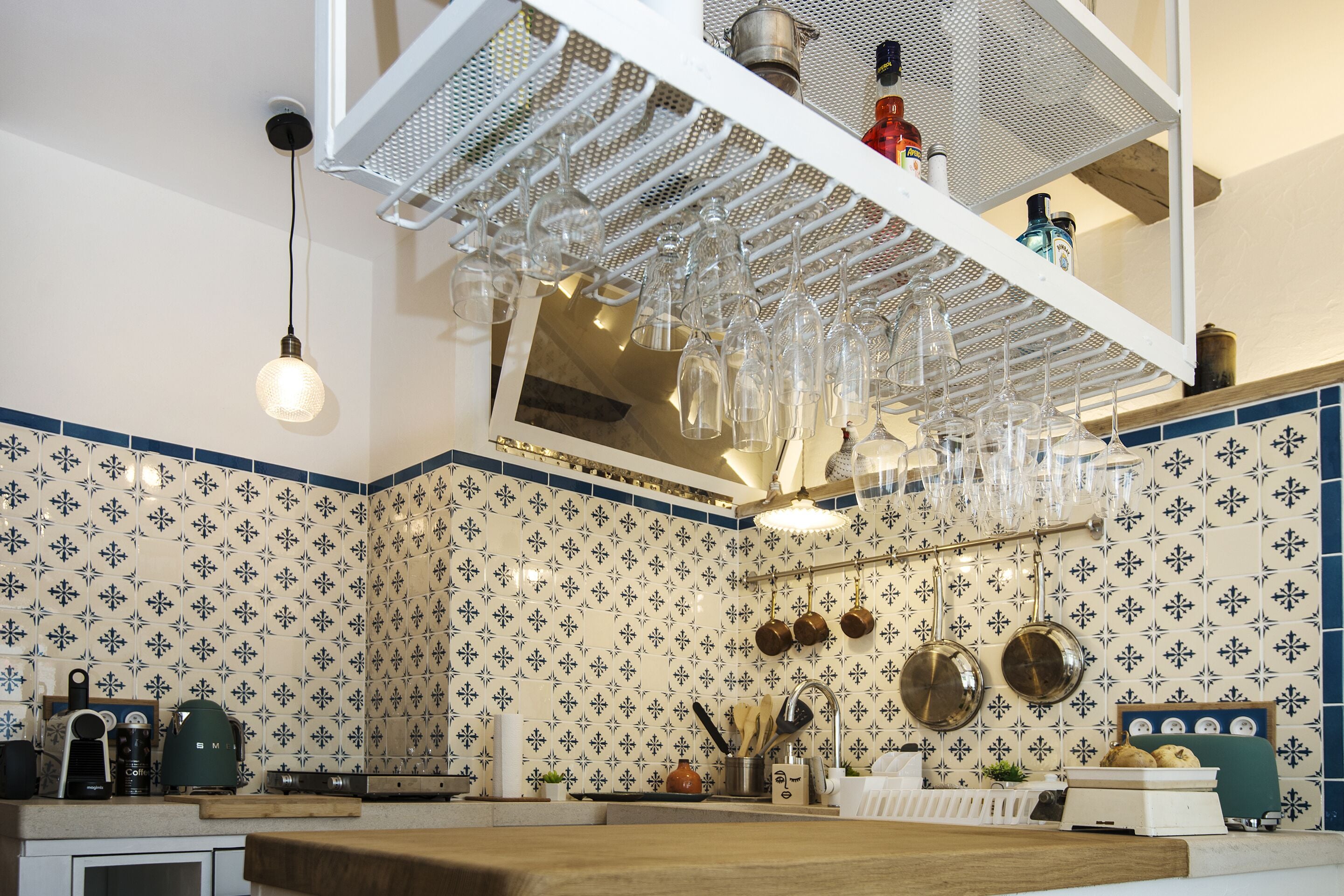 Una cocina con copas de vino colgando, una cafetera y una variedad de utensilios de cocina.