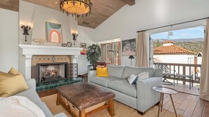 A living room with a fireplace, a sofa, an ottoman, and a balcony with a view of houses. - Superb La Vida Riviera 2 BD 2BA Gorgeous Riviera Views, Walk Everywhere! (Santa Barbara)