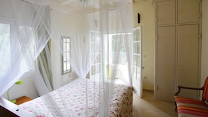 Un dormitorio con cama, una silla, un armario y una ventana con cortinas.