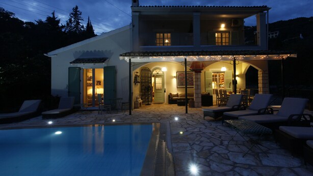 Una casa de dos pisos con piscina, mobiliario exterior y un interior bien iluminado.