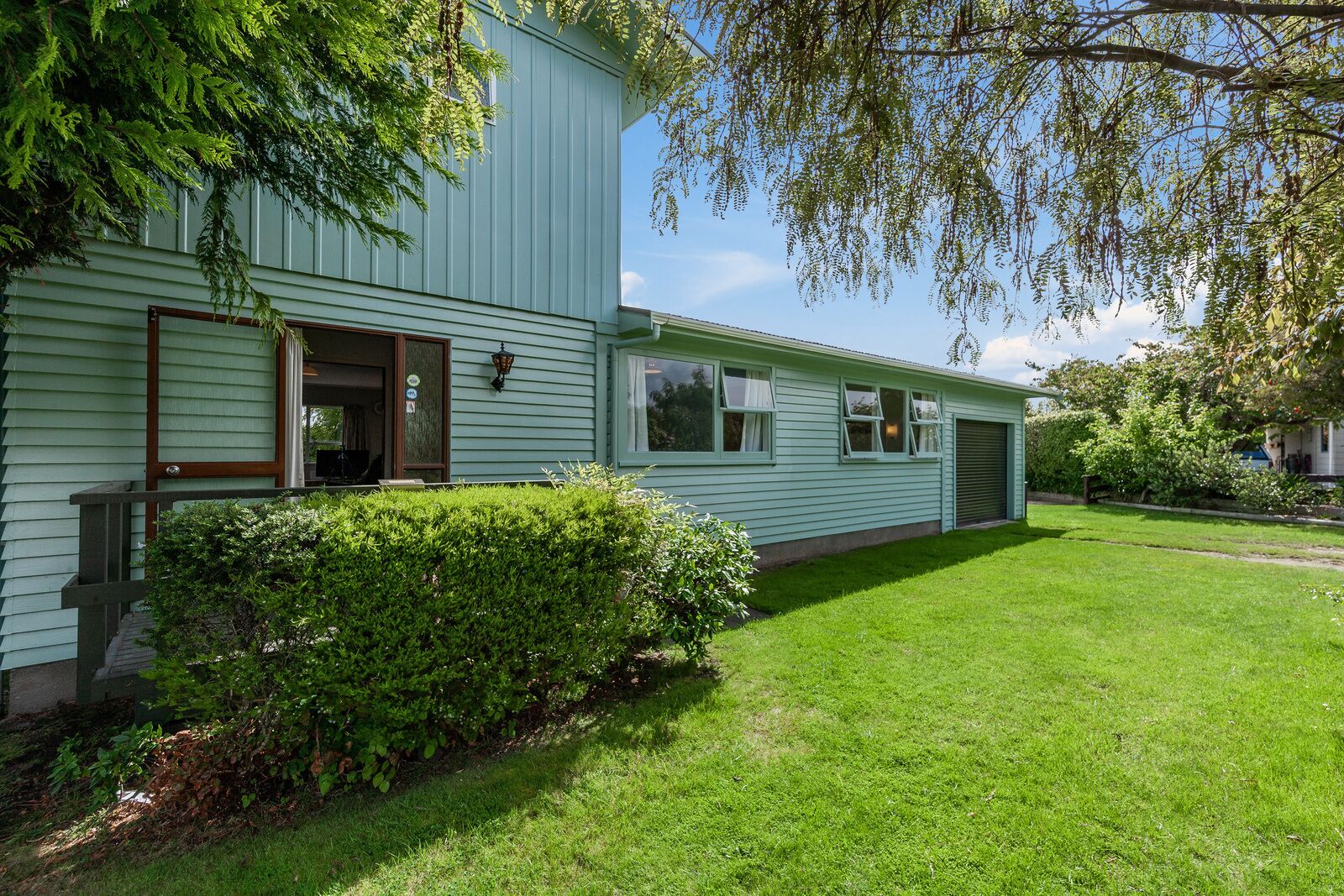 A light green two-story building with a front porch, a small garden, and a garage.