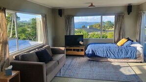 A bedroom with a bed, a TV, a sofa, and a window with a view of greenery. - Kapuka Paradise - Wharewaka Holiday Home (Wharewaka)
