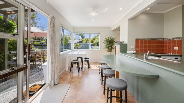 A modern kitchen with a bar area, large windows, and a dining area with a table and chairs. - Kapuka Paradise - Wharewaka Holiday Home (Wharewaka)