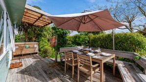 An outdoor wooden deck with a table set for dining, surrounded by lush greenery and a clear sky. - Kapuka Paradise - Wharewaka Holiday Home (Wharewaka)