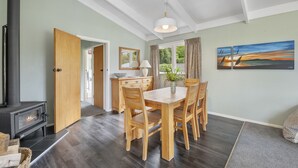Un coin repas avec une table et des chaises en bois, un poêle à bois noir et un tableau accroché au mur.