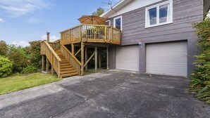 Une maison à deux étages avec une terrasse en bois, un garage et une pelouse bien entretenue.