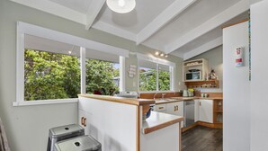 Une cuisine moderne avec des meubles blancs, un plan de travail en bois et une vue sur la verdure à l’extérieur.