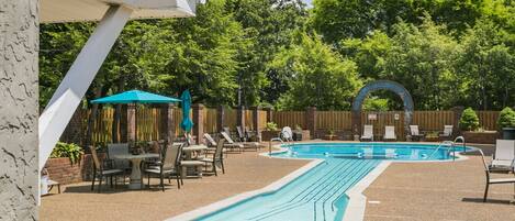 A rectangular swimming pool with a tiled deck, surrounded by lounge chairs and umbrellas.