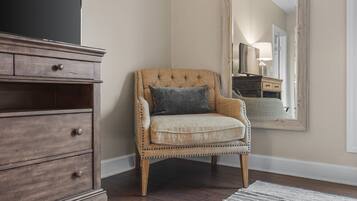 A corner room with a wooden dresser, a cushioned armchair, and a large mirror on the wall.
