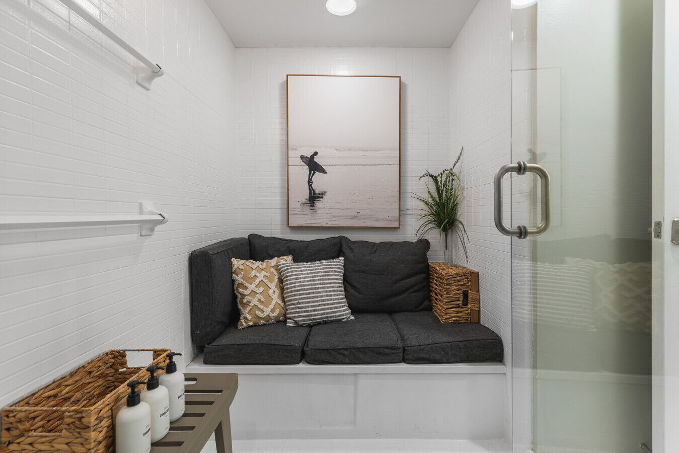 Un baño con sofá gris, un cuadro enmarcado, una planta y zona de ducha.