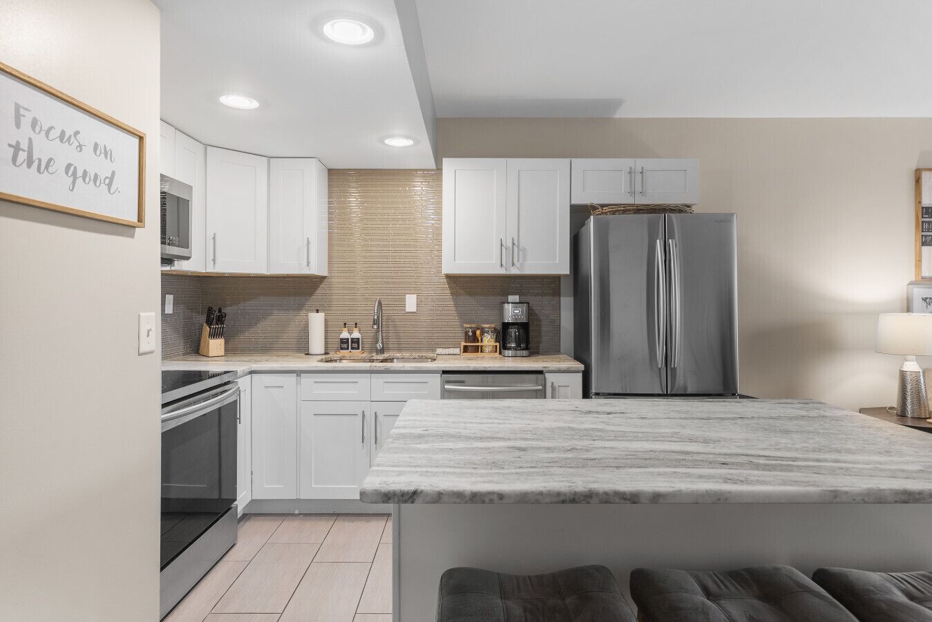 A modern kitchen with white cabinets, a stainless steel refrigerator, and a marble countertop.