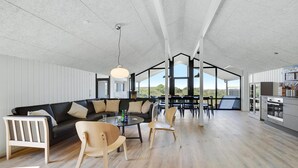 Ein geräumiger Wohnbereich mit schwarzem Sofa, Holzstühlen, einem Esstisch und einer Küchenzeile mit modernen Geräten.