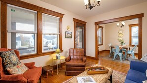 A living room with a brown leather armchair, a blue sofa, a wooden coffee table, and a dining area with a table and chairs.