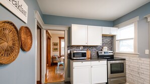 A modern kitchen with white cabinets, a microwave, stove, and a stone backsplash.