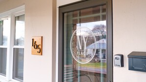 A building entrance with a glass door displaying a circular logo with "NY PLACE" and "Harrisonburg, Virginia" text. A wooden plaque with the number "165" is mounted on the wall.