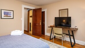 A bedroom with a bed, a desk with a chair, a television, and a door.