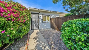 A residential property with a paved driveway, a wooden fence, and lush green foliage. - SD Getaway - Boho Studio, Spacious Yard w/ BBQ (San Diego)