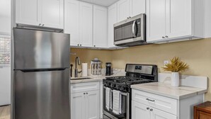 A modern kitchen with white cabinets, stainless steel appliances, and a wooden floor. - SD Getaway - Boho Studio, Spacious Yard w/ BBQ (San Diego)