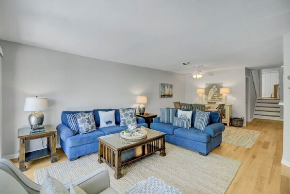 A living room with two blue sofas, a wooden coffee table, and a staircase leading to an upper floor. - Award-Winning Resort Amenities | Racquet Club 2 (Isle of Palms)