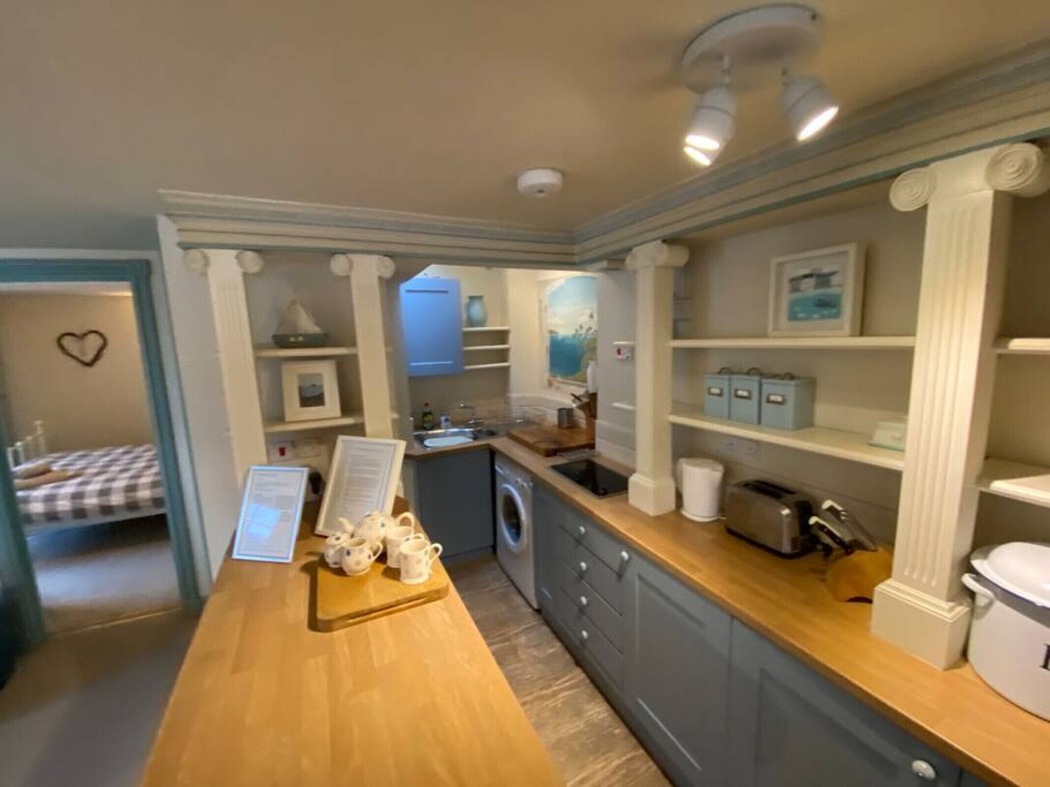 A compact hotel room with a kitchenette, a bed with a checkered bedspread, and a small bathroom.