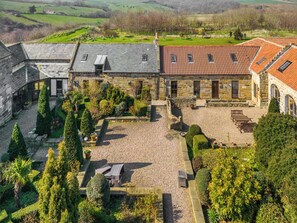 A courtyard with stone buildings, a gravel area, and neatly trimmed hedges.