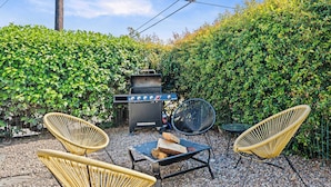 An outdoor patio with a barbecue grill, wicker chairs, and a table.