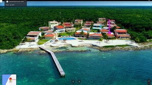 An aerial view of a coastal resort with multiple buildings, a pier, and clear turquoise waters.