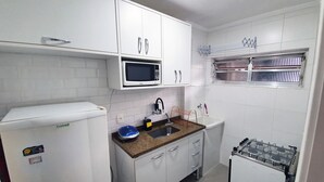 A compact kitchen with white cabinets, a microwave, a sink, and a gas stove.