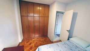 A bedroom with a wooden wardrobe, a bed with floral bedding, and a herringbone-patterned wooden floor.