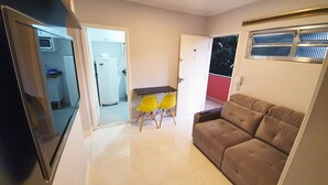 A compact living space with a kitchenette, a dining area with yellow chairs, and a brown sofa.