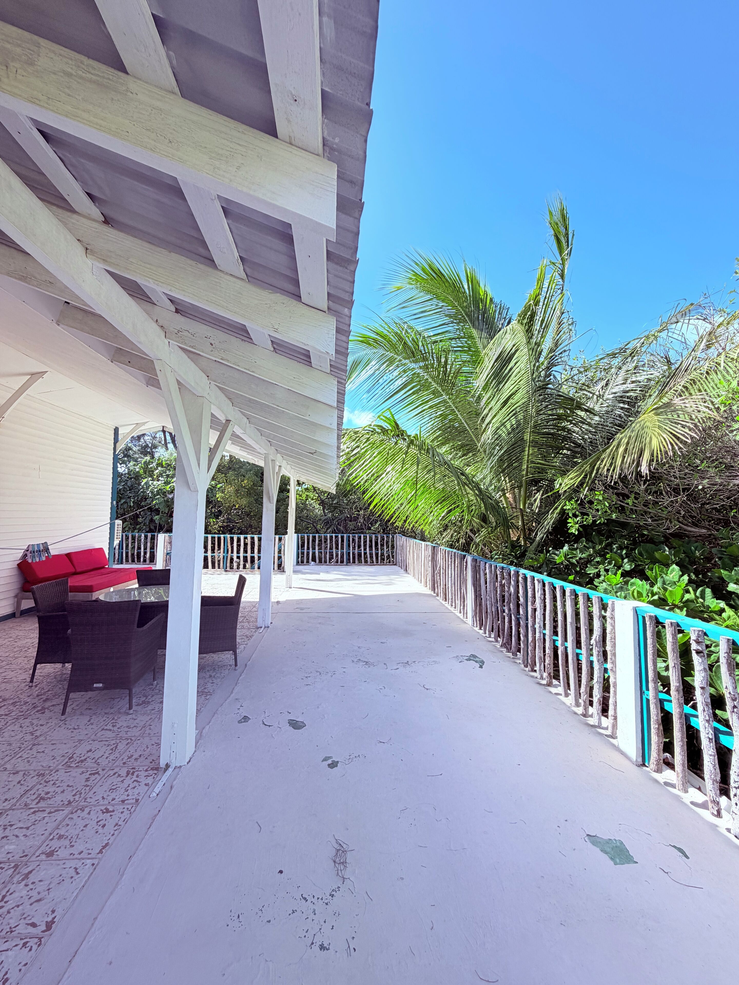 A covered outdoor area with a table and chairs, a red sofa, and a blue railing.