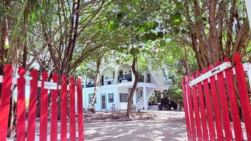 Un sentiero conduce a un edificio con facciata bianca, circondato da alberi e una recinzione rossa.