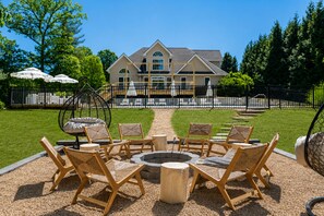 A patio with outdoor furniture and a fire pit, surrounded by a fence and a lawn.