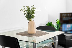 A modern dining area with a glass table, a beige vase with green plants, and a black chair. - Luxury One Bed - City Centre  - Secure Parking (West Midlands)
