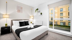 Ett modernt hotellrum med en stor säng, sänglampor, utsikt över en byggnad genom ett stort fönster och ett element på väggen.