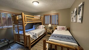 Une chambre avec deux lits superposés, une table de chevet avec une lampe et une fenêtre avec des stores.