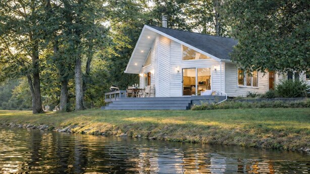Un chalet au bord du lac, doté d’une terrasse, de grandes fenêtres et offrant une vue sur l’eau.