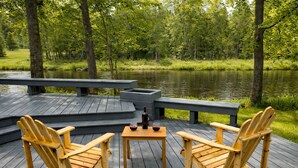 Une terrasse en bois avec des fauteuils Adirondack, une petite table et une bouteille de vin.