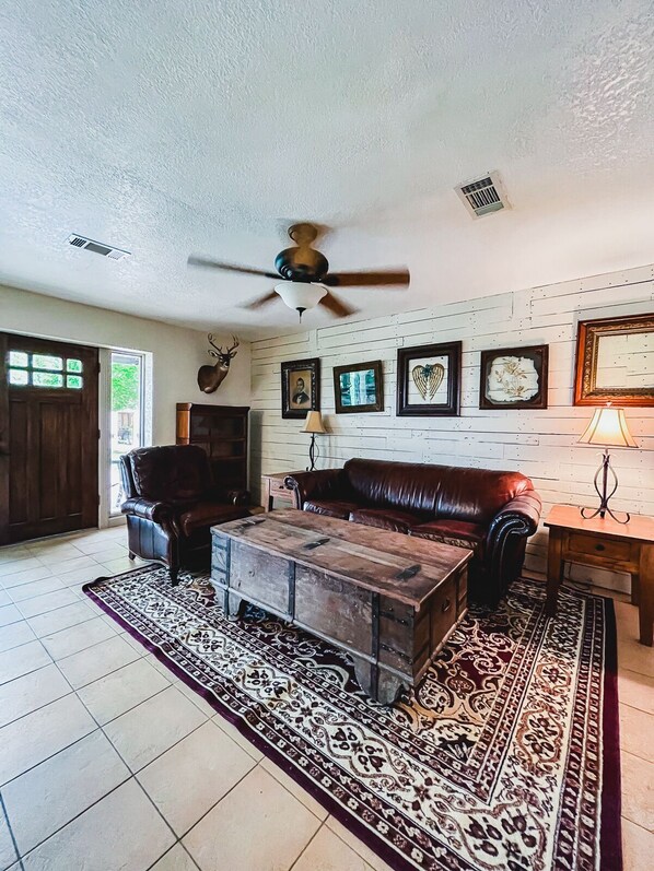 A living room with a fireplace, leather furniture, a ceiling fan, and a patterned rug.